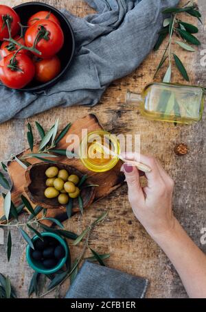 Draufsicht auf die weibliche Ernte, die Olivenöl aus dem Glas nimmt Jar beim Kochen köstlichen Salat mit reifen roten Tomaten an Holztisch Stockfoto