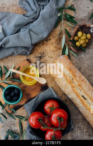 Draufsicht Zusammensetzung von frischem hausgemachtem Brot Laib auf gelegt Holztisch in der Nähe reifen roten Tomaten mit grünen und schwarzen Oliven und Olivenöl Stockfoto