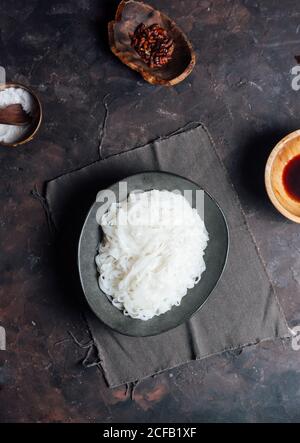 Draufsicht auf Schüssel mit gekochten Reisnudeln Tisch neben Schüsseln mit Sauce und Gewürzen bei der Zubereitung von Speisen In der Küche Stockfoto