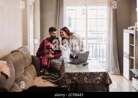 Fröhliche Schwangere und Ehemann verbringen Zeit zu Hause und Spaß beim Spielen mit Hund in rosa Kostüm gekleidet Stockfoto