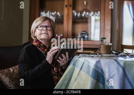 Ältere Frau schaut und berührt den Bildschirm des Smartphones, während sie auf dem Sofa im Wohnzimmer sitzt Stockfoto