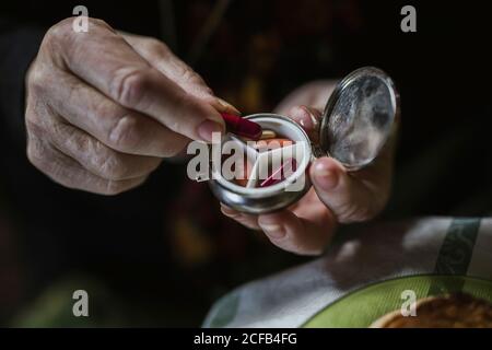 Hand einer älteren Frau, die eine rote Pille aus einer Pillenbox aus Stahl nimmt Stockfoto