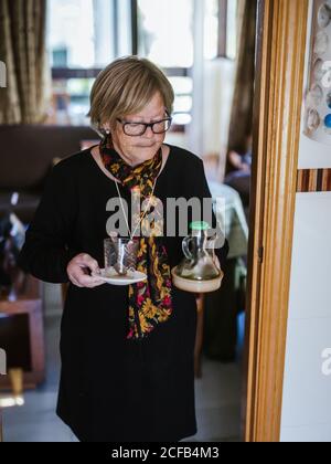 Eine ältere Frau hält sich in den Händen eine Glaskanne und einen Krug, während sie durch das Haus geht Stockfoto