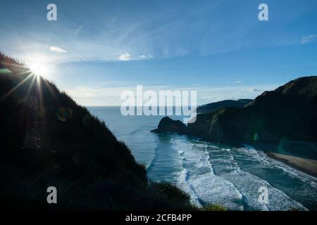 Blick vom Whites Strandweg über die Hügel mit Sonnenstrahlen, die über den Bäumen scheinen. White Beach ist vom nördlichen Ende des Piha Beach, Auckland Stockfoto
