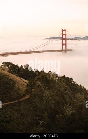 Atemberaubende Aussicht auf die majestätische Golden Gate Bridge über die neblige Meerenge Zwischen grünen Ufern gegen bunten Himmel in San Francisco in Kalifornien an warmen Abend Stockfoto