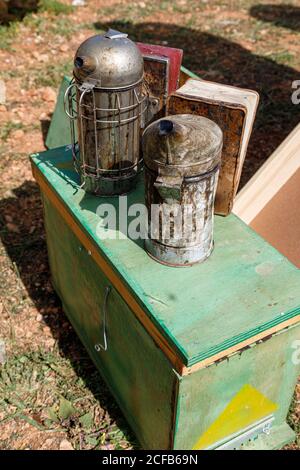 Von oben von alten Metallbienenrauchern auf Grün gelegt Hölzerne Bienenstock-Box in Bienenhaus in sonnigen Sommertag Stockfoto