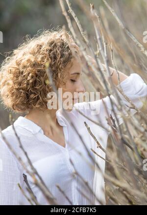 Seitenansicht Junge attraktive charmante Frau in der Nähe von trockenen Ästen von Strauch auf verschwommenem Hintergrund Stockfoto