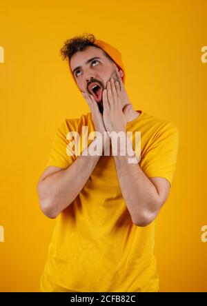 Bärtig trendy Mann in gelben Outfit macht lustige Gesicht gestikulieren Überraschung, die vor hellem gelben Hintergrund aufsteht Stockfoto