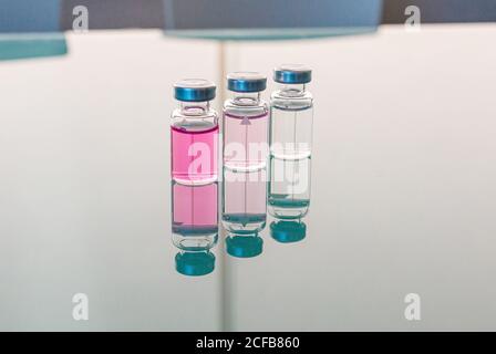 Reihe von transparenten Kolben mit rosa Flüssigkeit in Glas reflektiert Tabelle im biologischen Labor am Tag Stockfoto