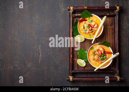 Garnelen Tom Yam Kung in weißen Schalen auf autentischem thai Tablett Draufsicht, Holzhintergrund. Stockfoto