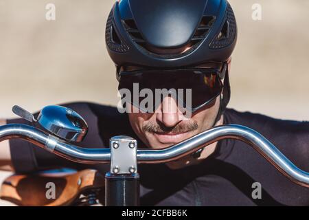 Portrait von glücklichen Mann in schwarz activewear und Helm suchen Bei der Kamera, während Sie mit Retro Penny Farthing Fahrrad auf stehen Rennbahn am Sportplatz Stockfoto