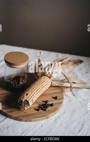 Getrockneter Mais auf dem Kot auf Holzbrett neben dem Glas gelegt Mit brauner Würze auf Küchentisch Stockfoto