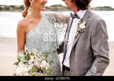 Crop unkenntlich jung zufrieden Paar in Hochzeitstag hinter stehen An leerer sandiger Küste Stockfoto