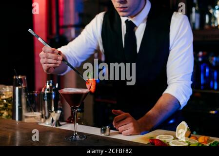 Junger eleganter Barkeeper, der hinter einer Theke arbeitet und Getränke vorbereitet In einem Glas Stockfoto