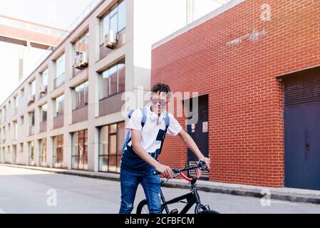 Junger lächelnder schwarzer erfolgreicher Mann mit Afro-Haaren in Casual Outfit und stylische Sonnenbrille stehen mit Fahrrad auf der Straße Stockfoto