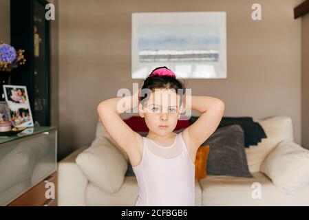 Liebenswert verärgert kleine Mädchen Tänzerin im Trikot suchen weg, während Haarbüscheltraining vor dem Balletttraining im gemütlichen Wohnzimmer Zu Hause Stockfoto