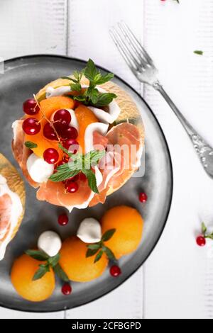Italienische Vorspeise mit Melone Prosciutto und Mozzarella Käse mit dekoriert Minzblätter und rote Johannisbeere Draufsicht Nahaufnahme Stockfoto