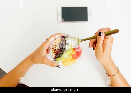 Von oben anonymen Weibchen genießen gesunde Gericht mit Früchten und Walnüsse über Tisch mit Smartphone im Restaurant Stockfoto