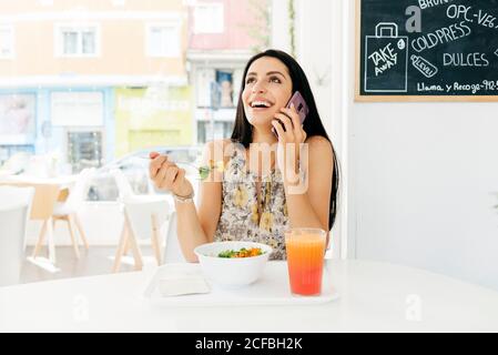 Fröhliche Frau mit gesundem Essen, die im Café auf dem Smartphone spricht Stockfoto