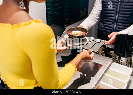 Crop African American Kellnerin geben Tablett mit Smoothie Schüssel und Löffel dienen Kunden über der Theke in einem kleinen Café Stockfoto