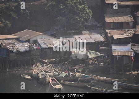 Blick vom Handelshafen auf die Kleinstadt in Freetown in Sierra Leone. Abgerissene und arme Häuser und hölzerne Fischerboote im Vorort der Hauptstadt. Stockfoto