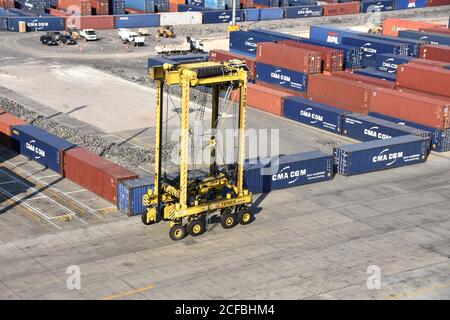 Ein Straddle Carrier im Kingston Freeport Terminal, der in der Nähe von Containern vorbeifährt. Der gelbe Sattelzug ist leer und bewegt sich zum Verladen in Richtung Schiffe. Stockfoto