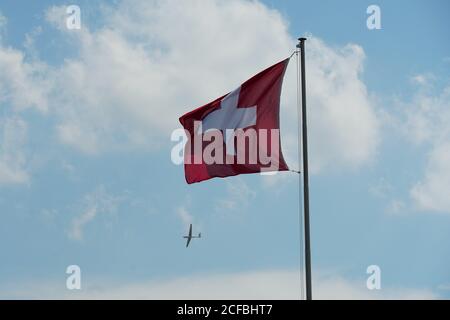 Schlagfahne der Schweiz zeigt ein weißes Kreuz in der Mitte eines quadratischen roten Feldes. Flagge ist am Fahnenmast befestigt und im Hintergrund ist Segelflugzeug. Stockfoto