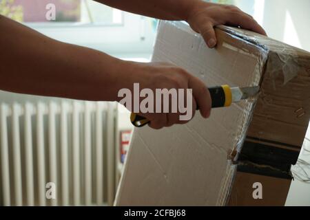 Ein Mann, der ein Papppaket mit Möbelteilen für die DIY-Montage öffnet. Nahaufnahme Foto mit Details über den Arbeitsprozess für die Verbesserung seiner Heimat. Stockfoto