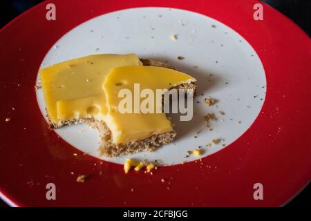 Ein Käse-Sandwich übrig gessenen und mit Bissen herausgenommen Des Sandwiches auf einer roten und weißen Platte mit Ein glatter Holzhintergrund Stockfoto