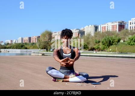 Junge afroamerikanische Fitness-Frau in Sport-Top und Leggings Sitzen und Stretching beim Entspannen nach hartem Training in der Stadt park im Sommer sonnigen Tag Stockfoto