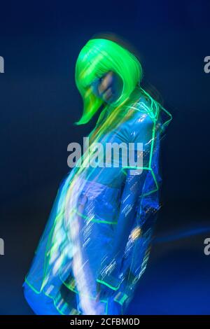 Junge asiatische Frau in gelber Perücke und transparentem Kunststoff tragen posiert in fluoreszierendem Licht Stockfoto