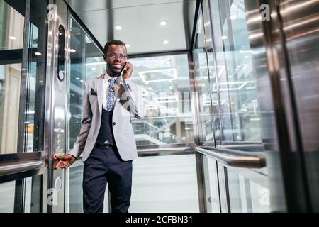 Portrait von afroamerican Geschäftsmann in der modernen Aufzug aus Glas am Telefon sprechen Stockfoto