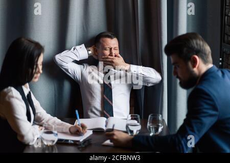 Geschäftsmann gähnt mit Kollegen, die ihn während des Meetings anguckend anschauten Konferenzraum Stockfoto