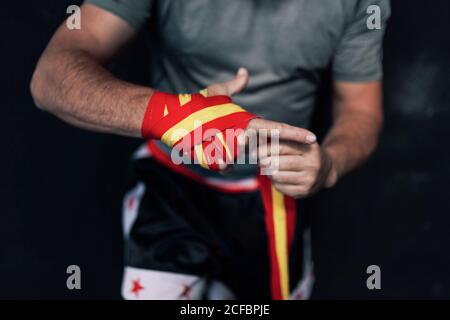 Cropped nicht erkennbarer männlicher Athlet in Sportswear, der sich an einem Riemen anlegt Handgelenk, während man gegen die dunkle Wand steht und sich auf das Training vorbereitet Im Fitnessstudio Stockfoto