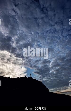 Der eineinige Wanderer steht auf dem Gipfel in einer Silhouette mit dramatischen Wolken. Stockfoto