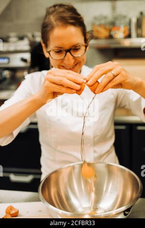 Weibliche Köchin knackt Eier in einer Restaurantküche, Lifestyle Nahaufnahme Foto Stockfoto