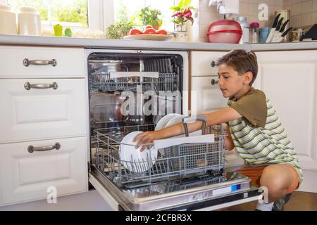 Kleiner Junge, der die Spülmaschine zu Hause beladen hat Stockfoto