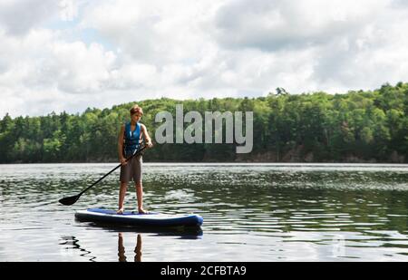 Teen boy paddeln auf einem SUP auf See in Ontario, Kanada an einem sonnigen Tag. Stockfoto