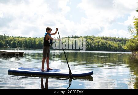 Teen boy paddeln auf einem SUP auf See in Ontario, Kanada an einem sonnigen Tag. Stockfoto