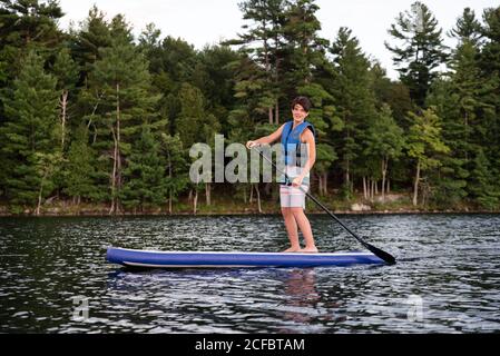 Teen boy paddeln auf einem SUP auf See in Ontario, Kanada an einem sonnigen Tag. Stockfoto