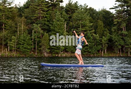 Teenager Junge fällt von einem Stand Up Paddle Board (SUP) auf einem See. Stockfoto