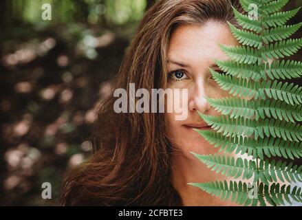 Porträt einer Brünette Frau, die ihr halbes Gesicht mit einem Farnblatt bedeckt. Stockfoto