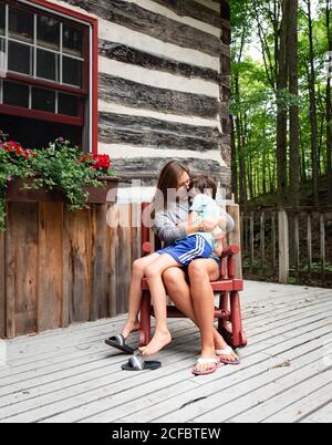 Mutter und Sohn sitzen im Schaukelstuhl auf Deck einer rustikalen Blockhütte. Stockfoto