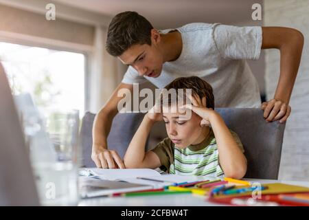 Teenager Junge hilft seinem jüngeren Bruder Hausaufgaben zu Hause Stockfoto