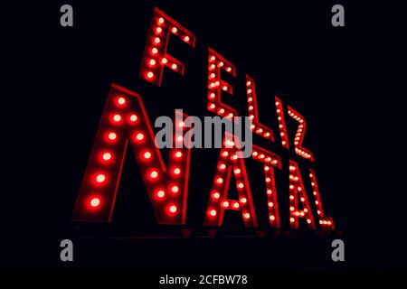Frohe weihnachten auf portugiesisch auf Neon-rotes Licht geschrieben. Weihnachtlicher schwarzer Hintergrund, Platz für Text. Stockfoto