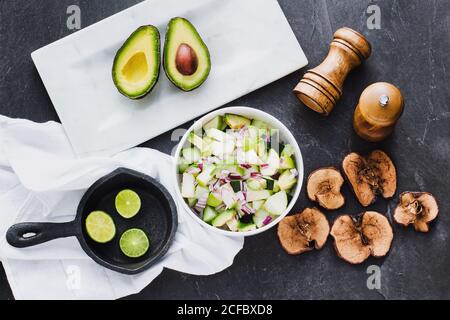 Draufsicht auf Schüssel mit köstlichem Avocado-Salat in Zusammensetzung Mit Kalk Hälften in Pfanne und schneiden Avocado mit gebraten apple Chips auf dem Tisch Stockfoto