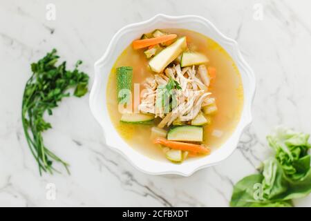 Serviert Schüssel mit Hühnersuppe mit Karotten, Koriander und Zucchini auf dem Tisch Stockfoto