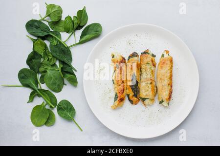 Draufsicht auf leckere Brötchen mit gebratenem Hähnchenfilet platziert Auf dem Teller neben frischen Spinatblättern auf hellgrauem Tisch Stockfoto