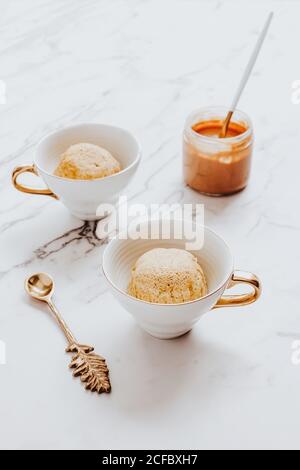 Tassen mit Eisschüsseln in der Nähe von dekorativen Löffel und platziert Glas Erdnussbutter auf Marmortisch Stockfoto