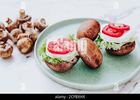 Hoher Winkel von gesunden Schalen mit Pilzen gefüllt mit Salat und Käse mit Tomatenscheiben auf grünem Teller serviert Stockfoto